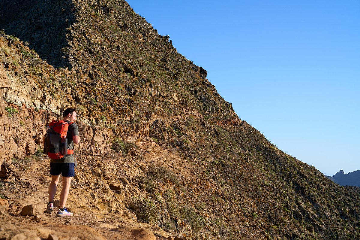 A hiker descending a steep ridge under the late afternoon sun.